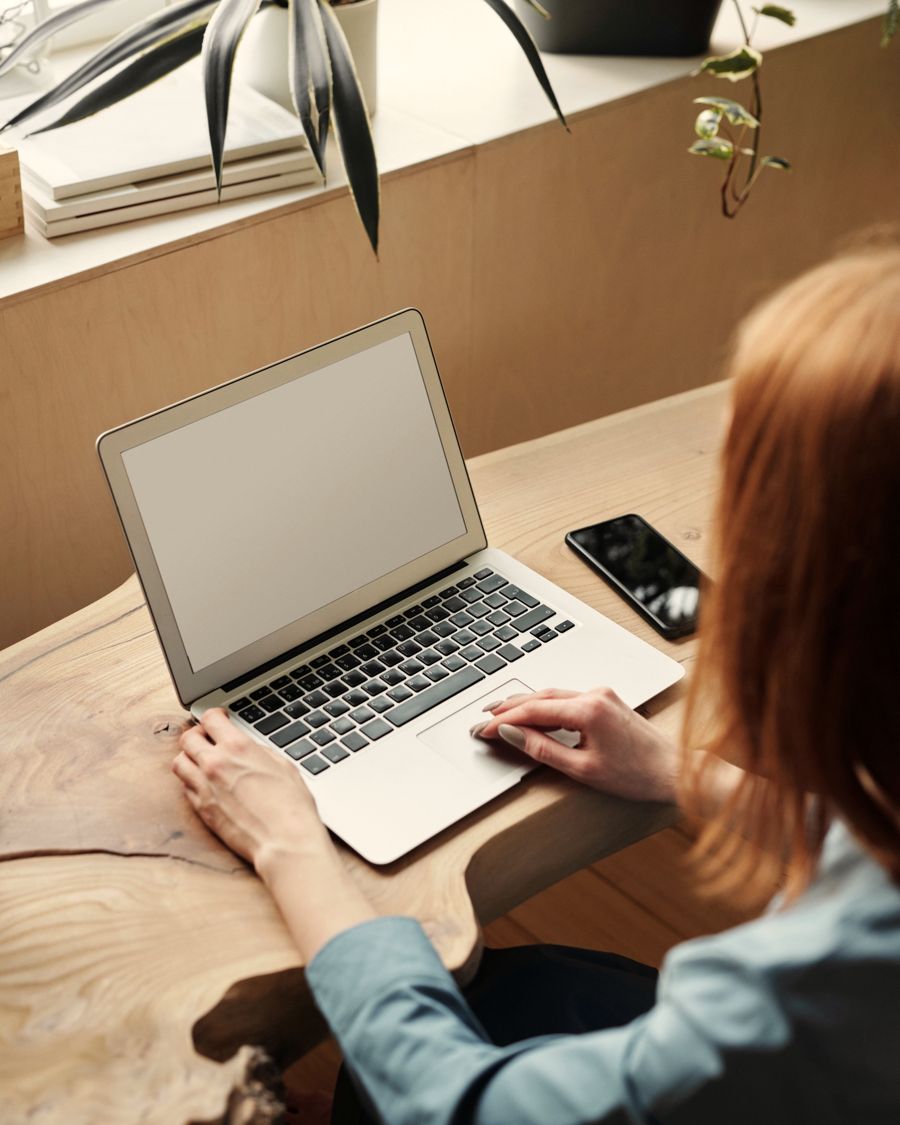 Mulher trabalhando no notebook em uma mesa de madeira, junto à janela